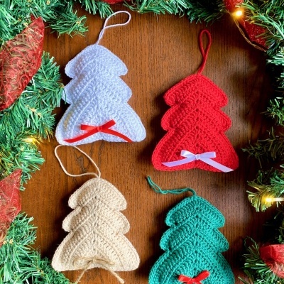 Enfeites de árvore de Natal em croché, cores branca, vermelha, bege e verde, com laços pequenos, sobre fundo de madeira e guirlanda decorativa.