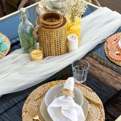 Mesa com decoração rústica, acessórios trançados naturais, talheres dourados e vasos de vidro