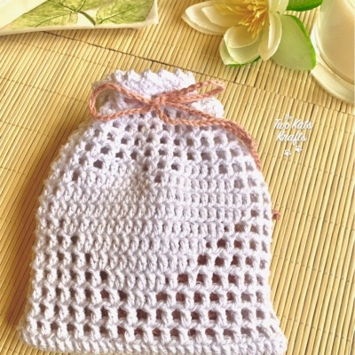 Saco branco em croché com cordão rosa num fundo de bambu com flor e porta-copos