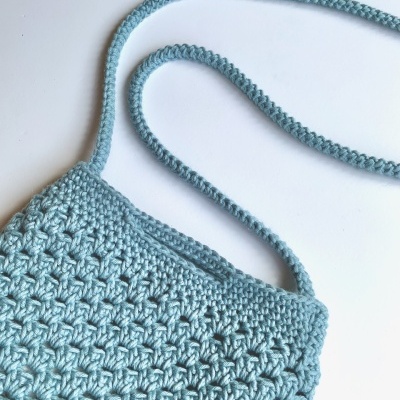 Bolsa azul de crochet com alça sobre fundo branco.