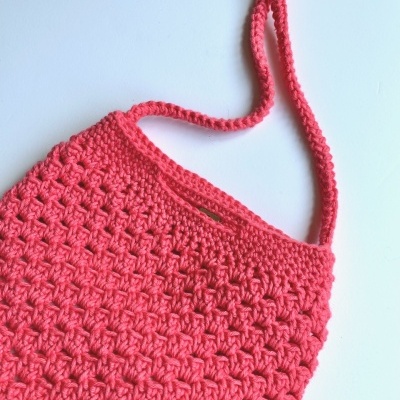 Bolsa rosa de crochê com alça fina sobre fundo branco