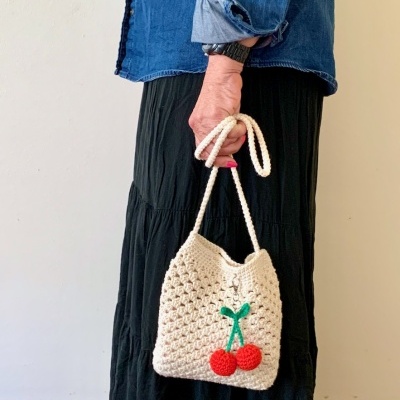 Mala pequena de crochet bege com cerejas vermelhas e folhas verdes na alça de cordão.