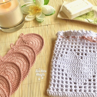 Discos de croché cor de rosa, bolsa de croché branca, vela, flor branca e sabonete sobre tapete de bambu.
