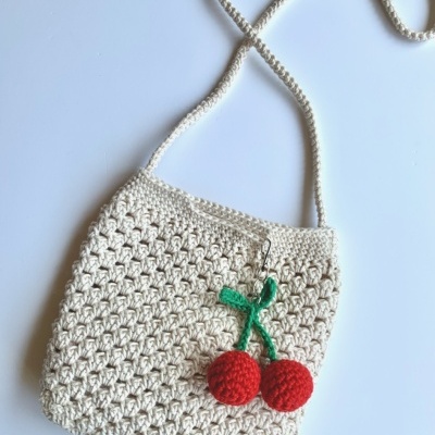 Bolsa em croché bege com chaveiro de cerejas vermelhas e verdes