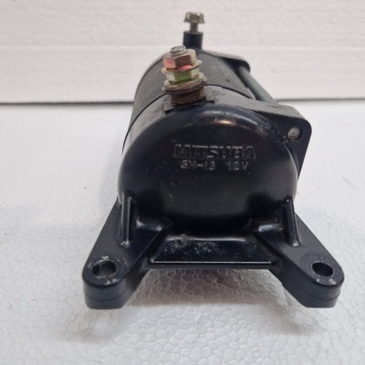 Peça automóvel preta de metal com suportes para fixação sobre superfície branca