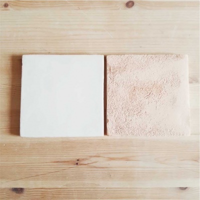 dois azulejos quadrados branco e bege com texturas diferentes sobre madeira