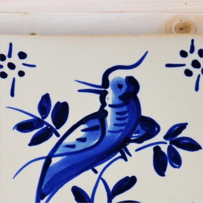 Azulejo cerâmico com pintura azul de pássaro e folhas, padrão geométrico nos cantos