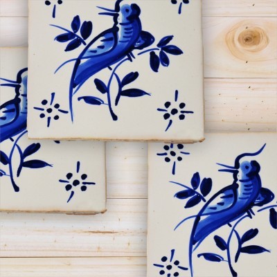 Azulejos cerâmicos brancos com desenhos de pássaros azuis sobre fundo madeira clara