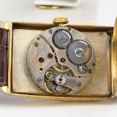 Mecanismo interno de relógio de pulso com caixa dourada e correia castanha