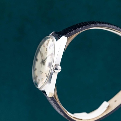 Relógio de pulso prateado com mostrador creme e bracelete preta de couro.