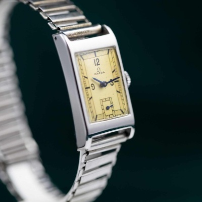 Relógio Omega de pulso com bracelete metálica e mostrador retangular creme.