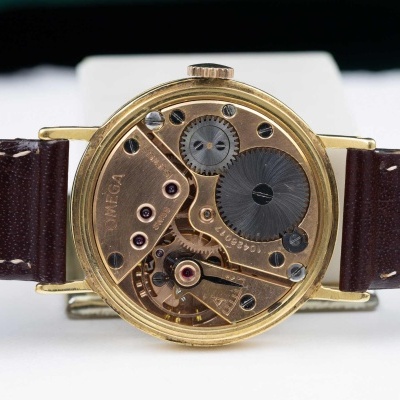 Relógio de pulso dourado com mecanismo interno exposto e pulseira em couro castanho