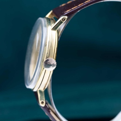 Relógio dourado com bracelete de pele castanha sobre fundo azul