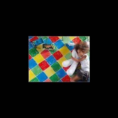 Criança desenhando num chão colorido com padrões de quadrados grandes.