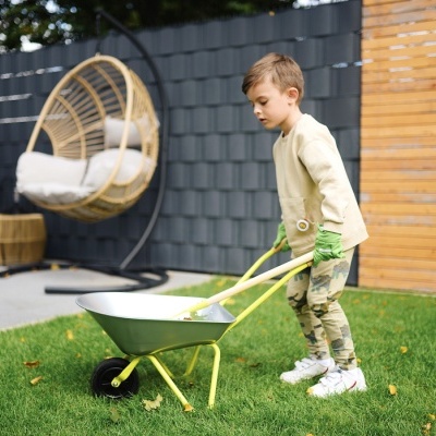 Menino a empurrar carrinho de mão metálico cinza com estrutura amarela num jardim