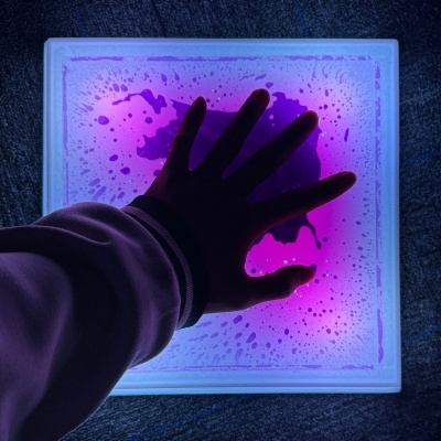 Mão sobre painel iluminado em roxo e rosa com padrão de gotas