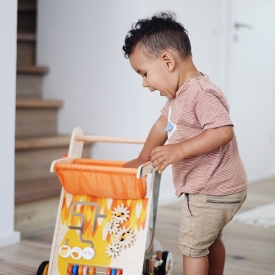 Menino empurrando carrinho de madeira para crianças com peças de atividades laranja
