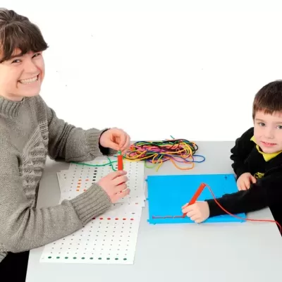 Mulher e criança usando tabuleiro azul com buracos e linhas coloridas numa mesa branca