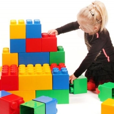 Criança brinca com blocos de construção coloridos sobre chão branco