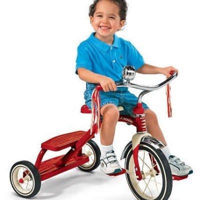 Criança em triciclo vermelho com franjas vermelhas no guiador