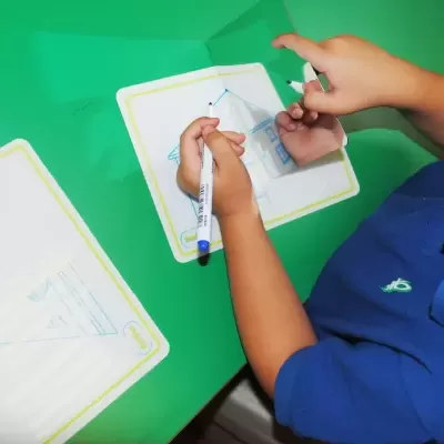 Criança desenha numa folha plástica transparente sobre mesa verde