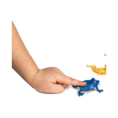 Mão da criança a pressionar sapo de plástico azul com outros sapos coloridos ao fundo.