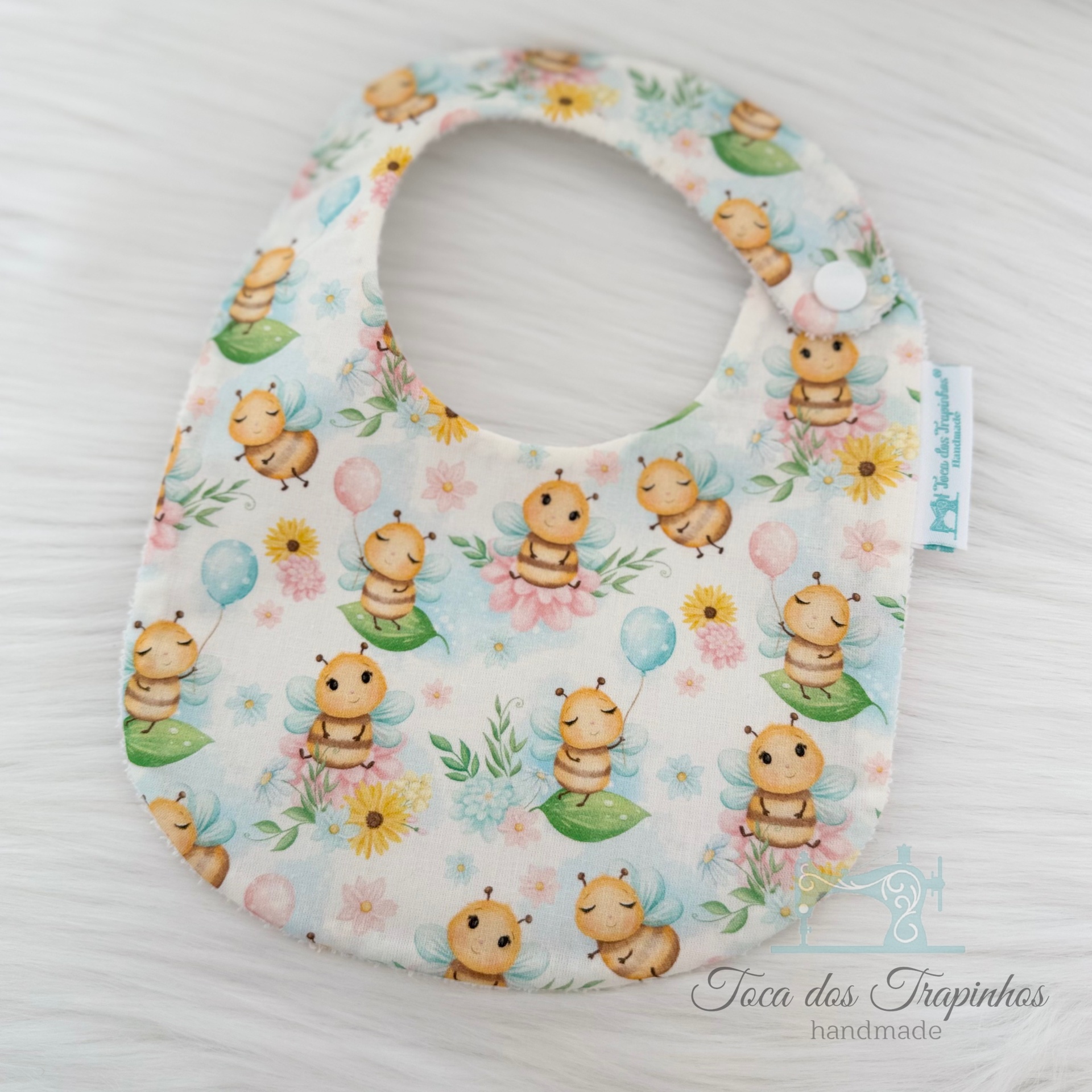 Babete infantil com padrão de abelhas, flores e balões em tecido branco