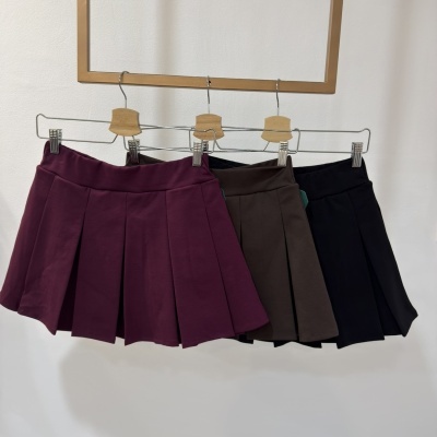 Três saias plissadas em cores bordo, castanho e preto penduradas em cabides.