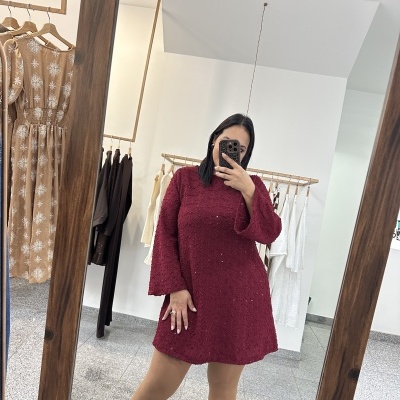 Mulher a usar vestido vermelho de malha com padrão texturizado e mangas largas em frente a espelho de madeira.