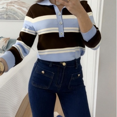 Mulher a usar camisola de malha azul, castanha e branca com calças de ganga escuras