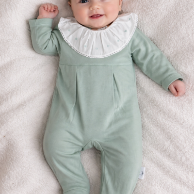 Bebé de macacão verde menta com gola branca bordada, deitado sobre manta branca felpuda