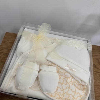 Conjunto de roupa de bebé branca numa caixa transparente com fita creme