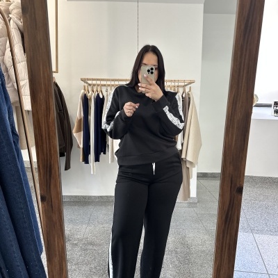 Pessoa com conjunto preto de sweatshirt e calças com faixa lateral branca a tirar foto num espelho