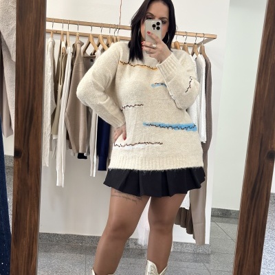 Mulher com camisola creme, saia preta e botas douradas a tirar selfie em espelho