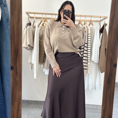Mulher tirando selfie com roupa bege e castanha diante de cabides com roupas