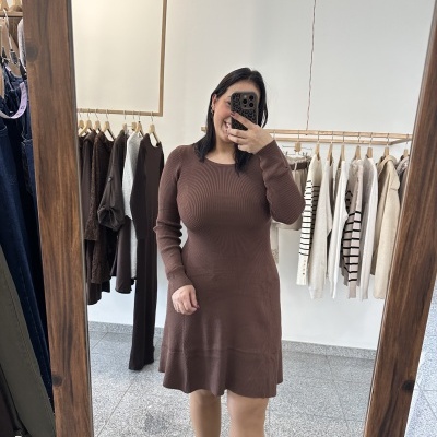 mulher a tirar selfie no espelho com vestido de malha castanho e roupas penduradas ao fundo
