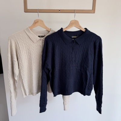 Polos de malha bege e azul escuro pendurados em cabides de madeira