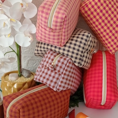 Necessaires xadrez coloridas dispostas com cosméticos e planta artificial ao fundo