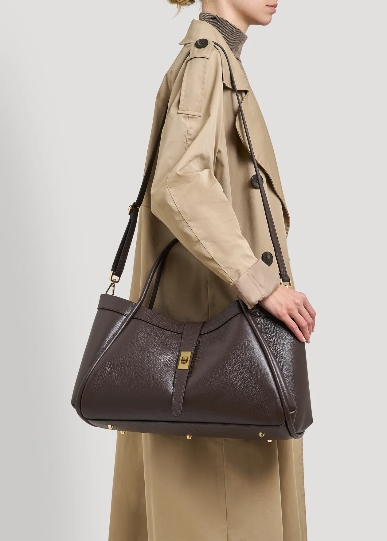 ROMA - CHOCOLATE Mala de pele castanha escura com fecho dourado na mão de pessoa com casaco bege