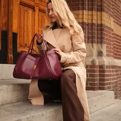 Mulher sentada segurando mala de mão marsala junto a porta de madeira