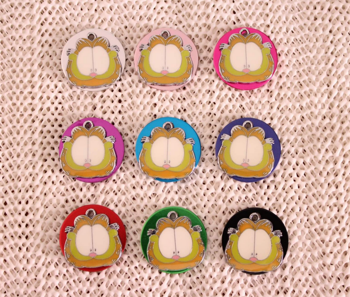 Nove pins do gato Garfield em várias cores sobre superfície texturada bege