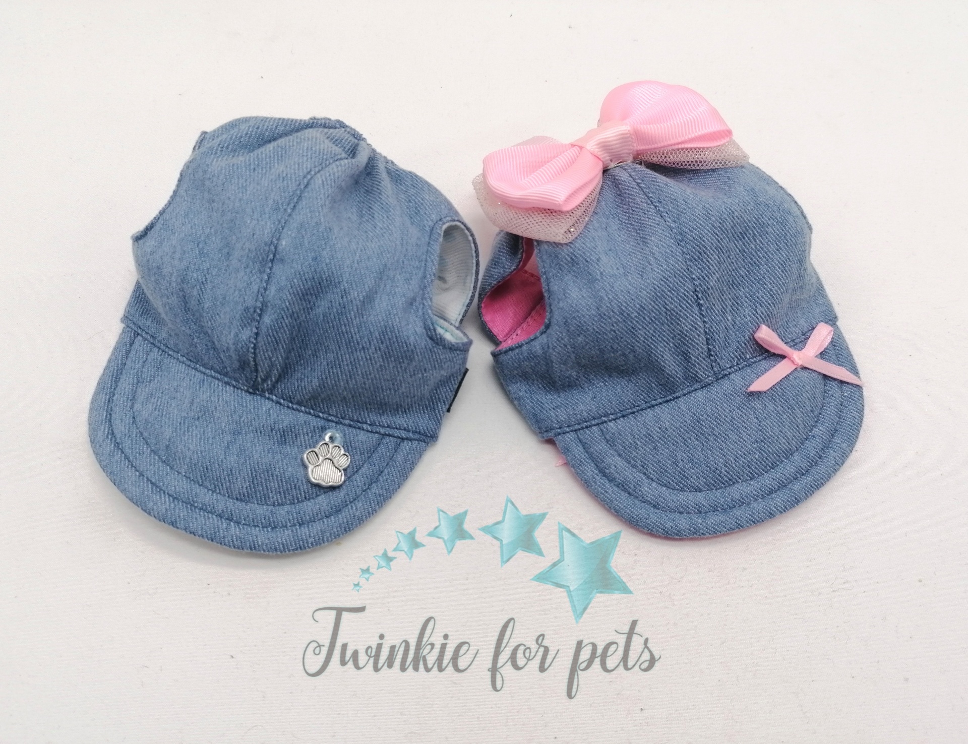 Dois bonés pequenos para cães azuis em tecido jeans com laços cor de rosa e texto da marca em fundo branco