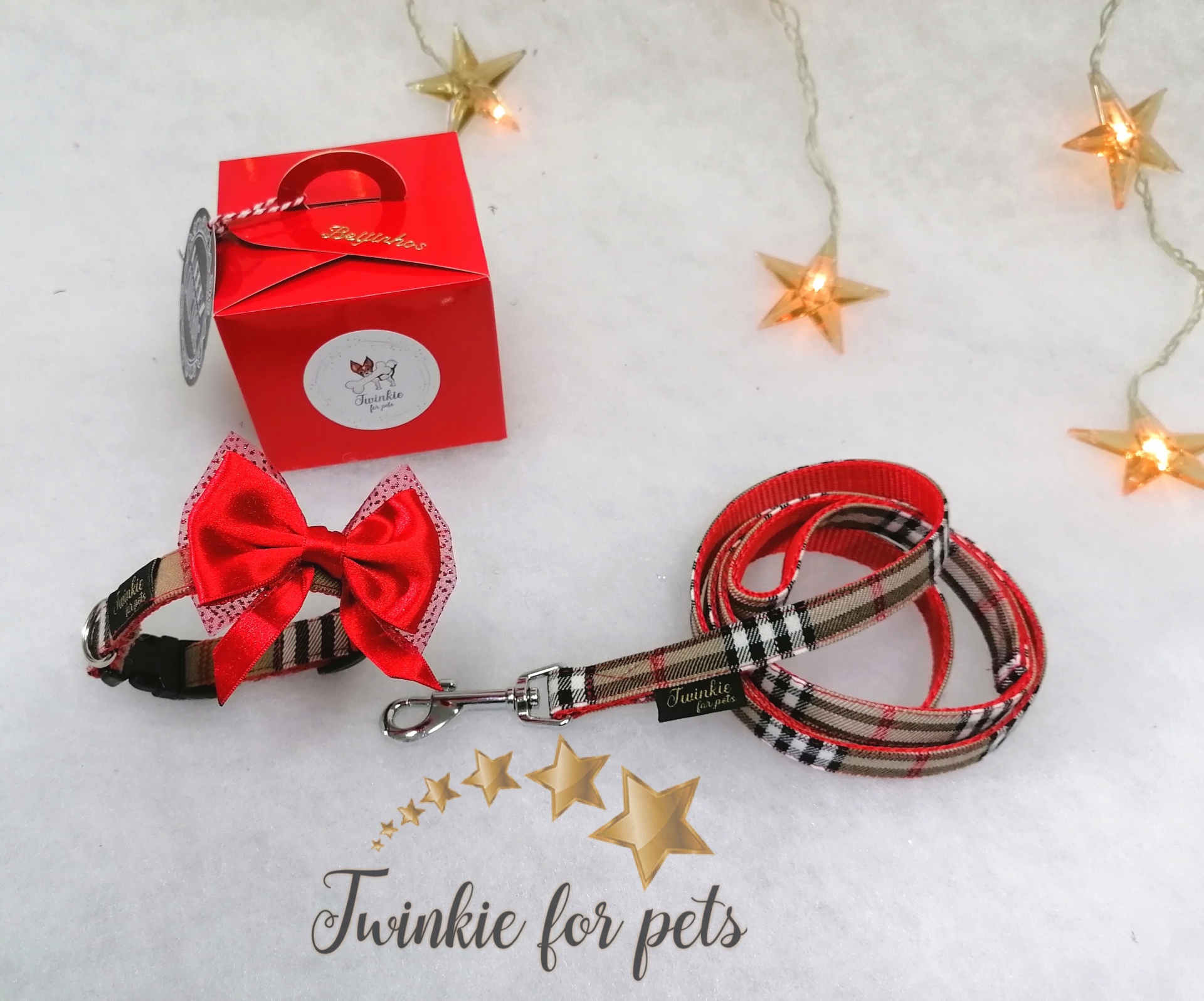 Conjunto trela e coleira xadrez com laço vermelho e caixa vermelha sobre fundo branco com estrelas.
