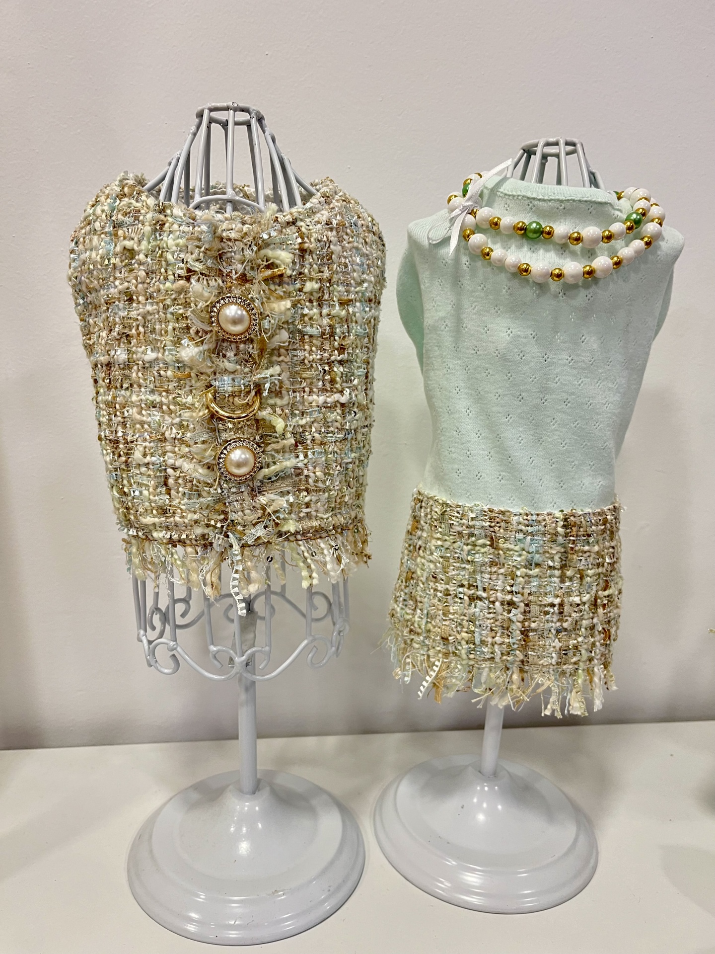 Dois manequins com roupas em tecido bouclé bege e verde claro com colar de contas