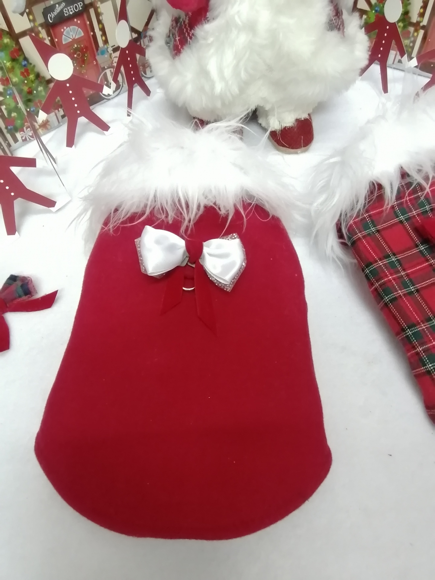 Capa vermelha para cão com laço branco e pelúcia na gola em cenário natalício