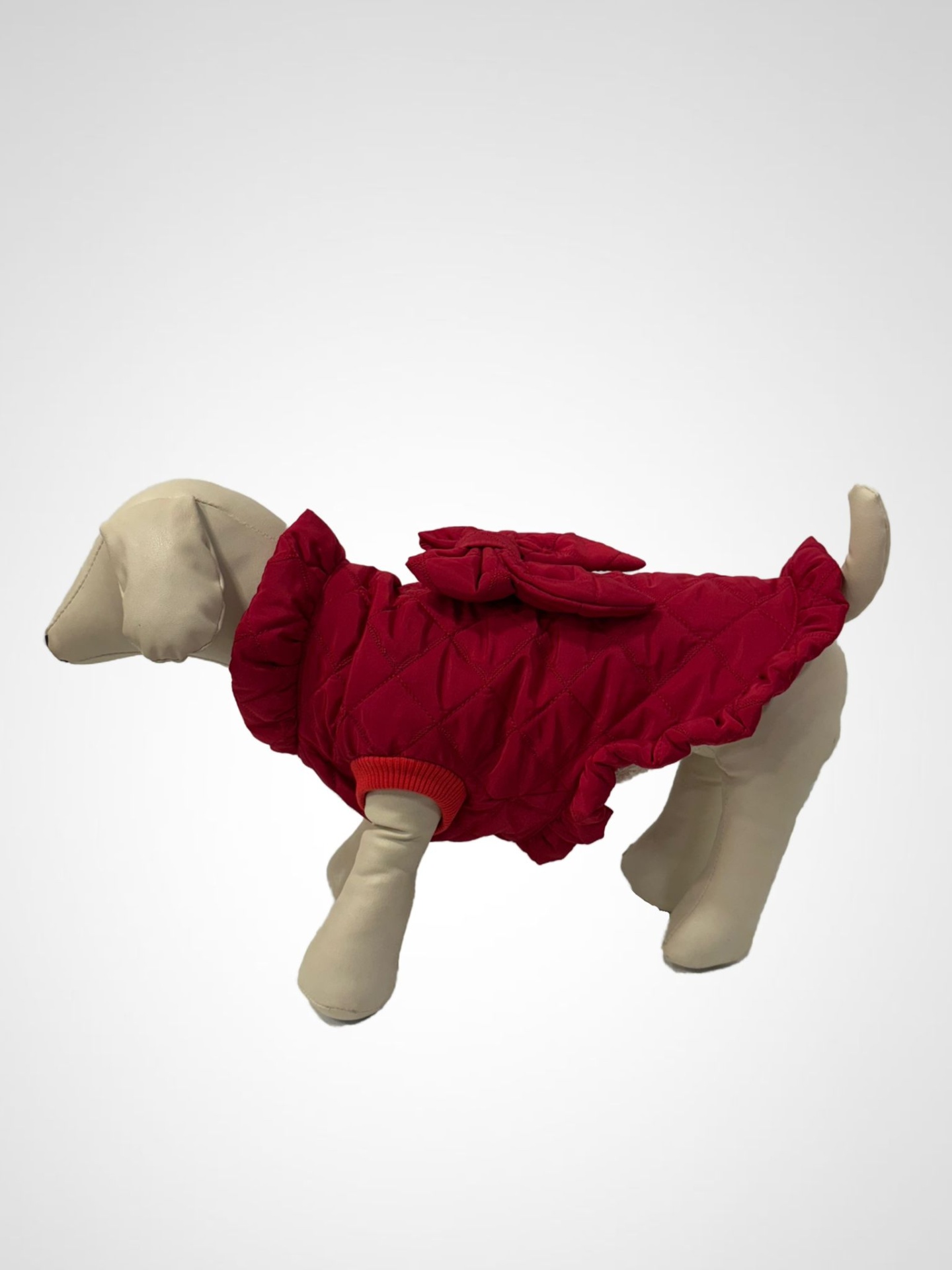 Roupa acolchoada vermelha para cão com laço decorativo num manequim.