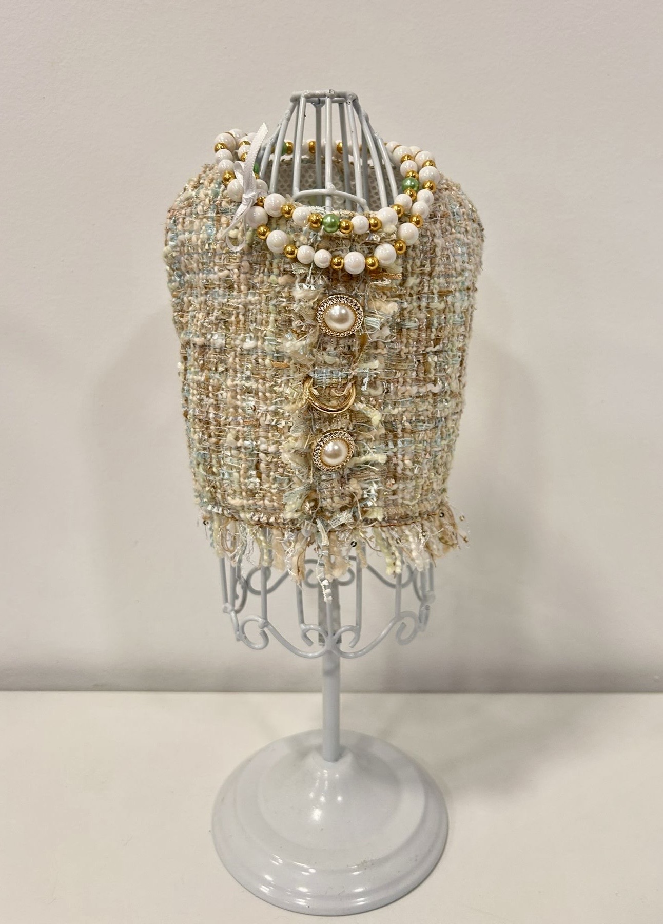 Colete tweed bege com botões de pérola num manequim branco