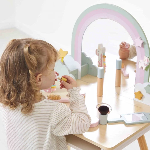 Criança a usar um espelho de maquilhagem de madeira colorido com acessórios sobre mesa clara