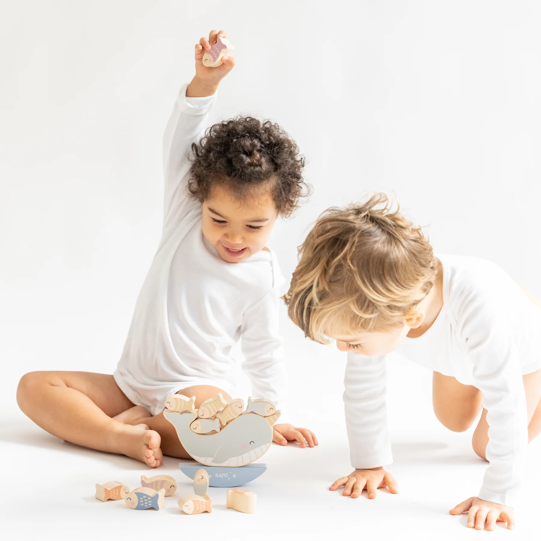 Duas crianças brincando com brinquedos de madeira coloridos num ambiente branco e iluminado