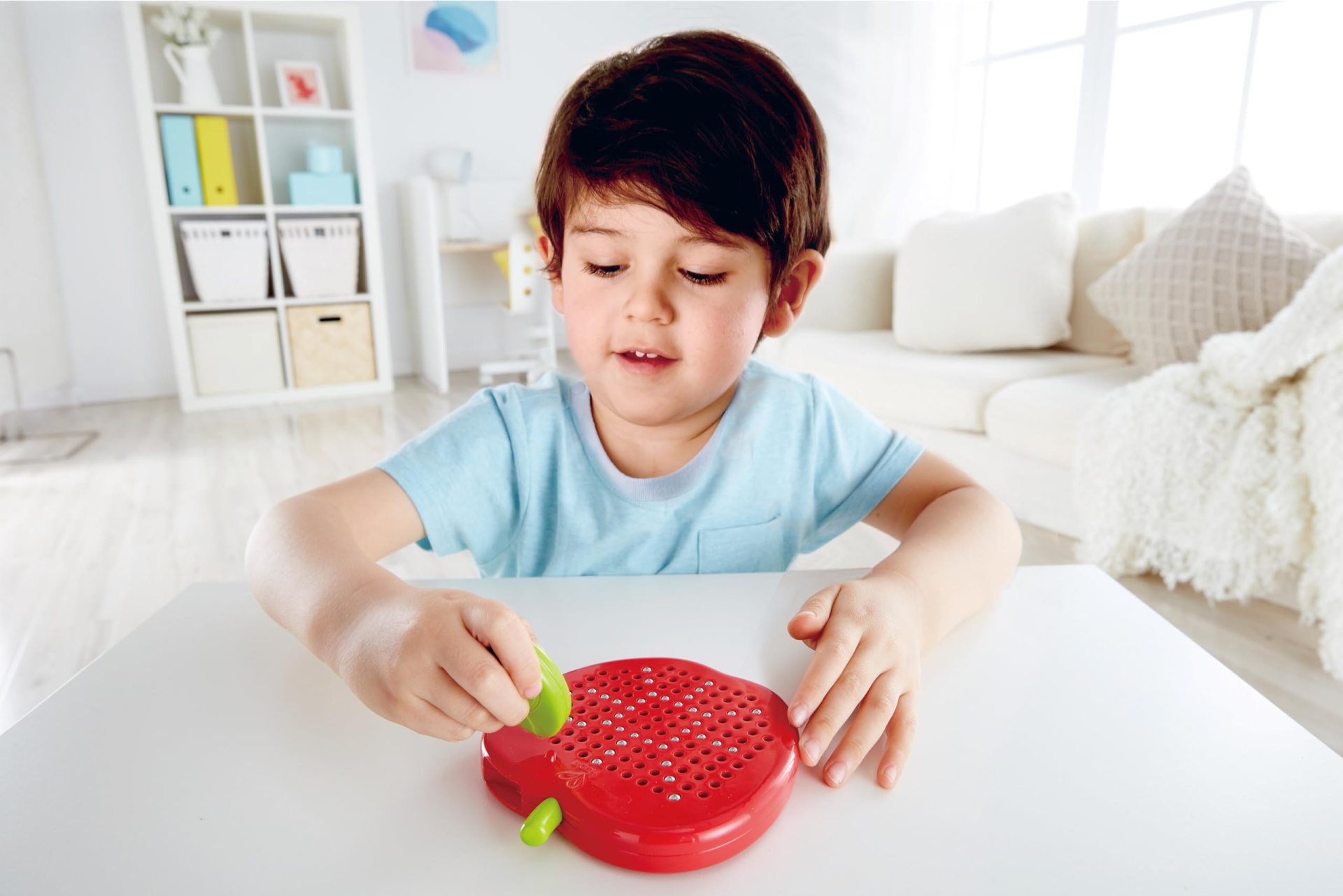 Criança a brincar com brinquedo vermelho em forma de maçã numa mesa branca